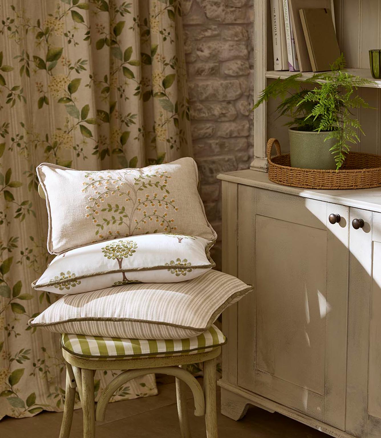 Close-up of stacked cushions showing mixed fabric designs, from textured neutrals to printed tree patterns and subtle stripes, with piped edges adding definition.