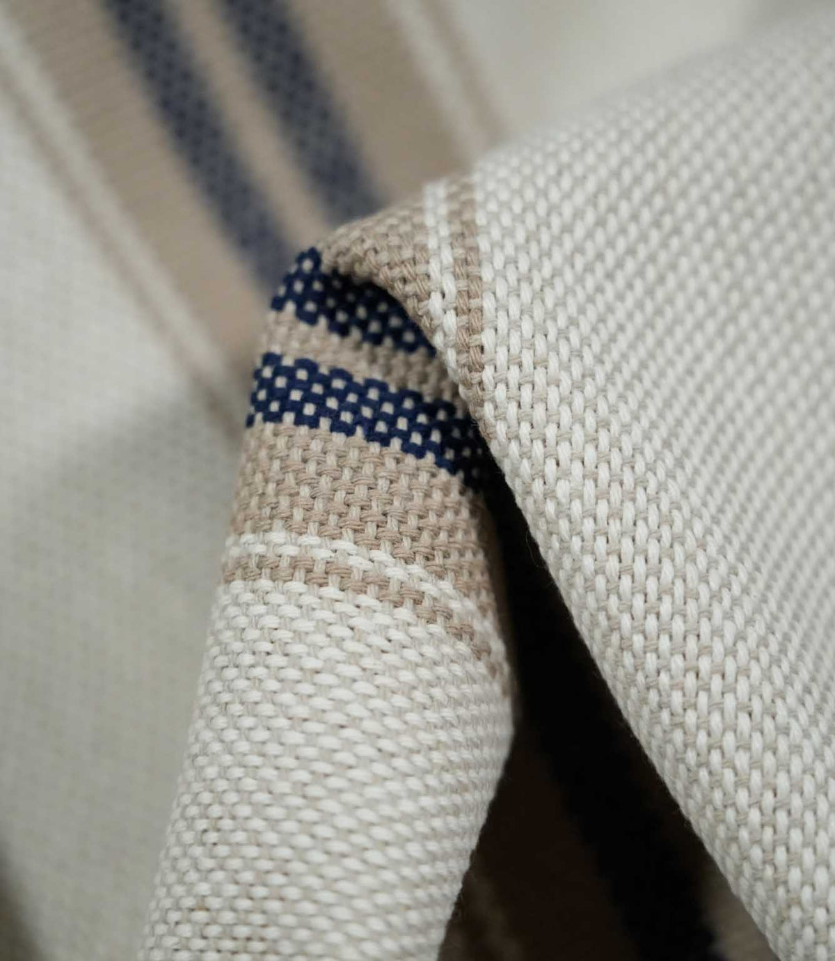 Macro close-up of folded Alma Stripe Marina fabric showing the detailed off-white weave and navy blue stripes set within a natural beige band.