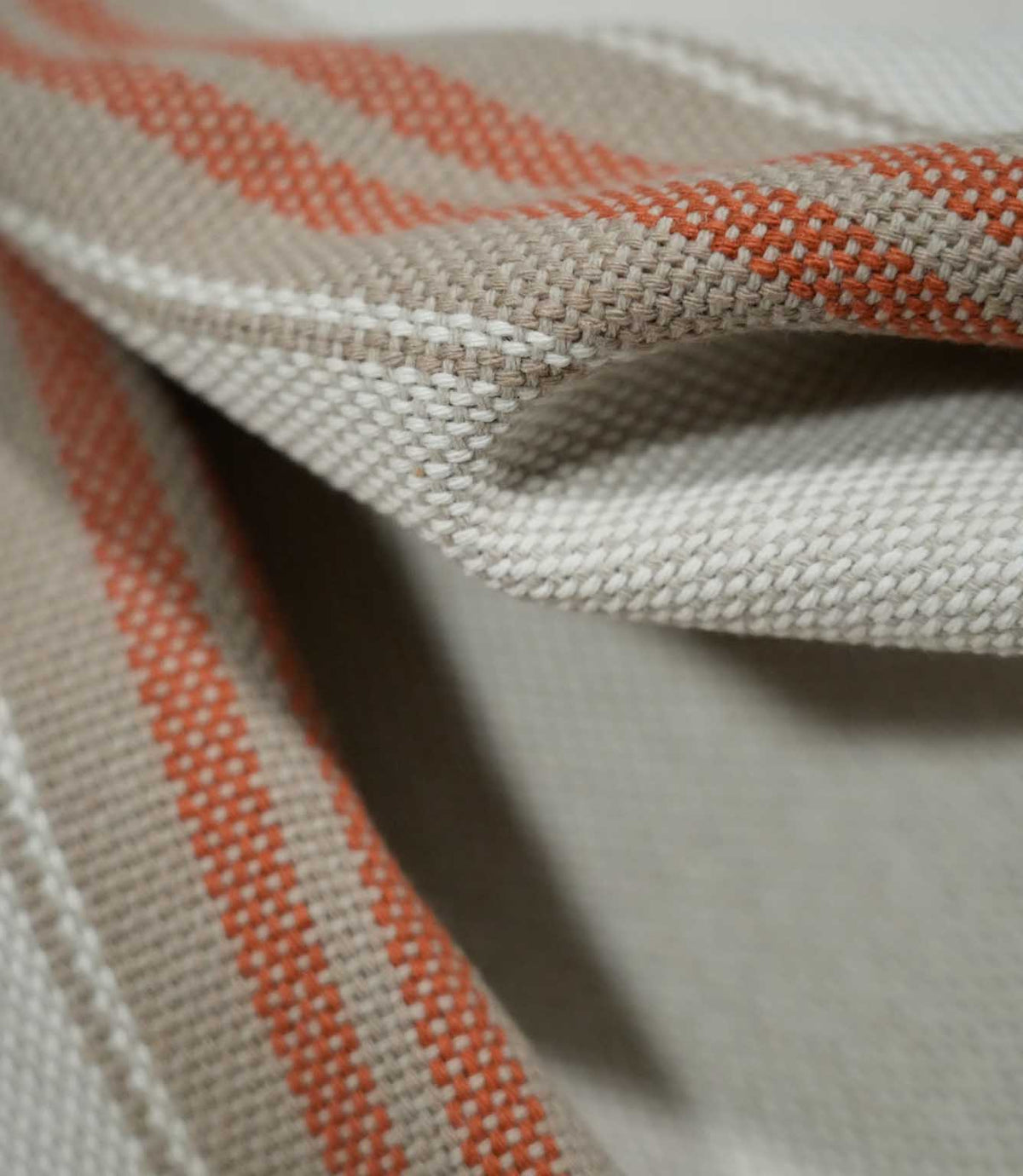 Close-up of folded Alma Stripe Terracotta fabric highlighting the substantial woven texture and terracotta stripes bordered by natural beige and off-white detailing.