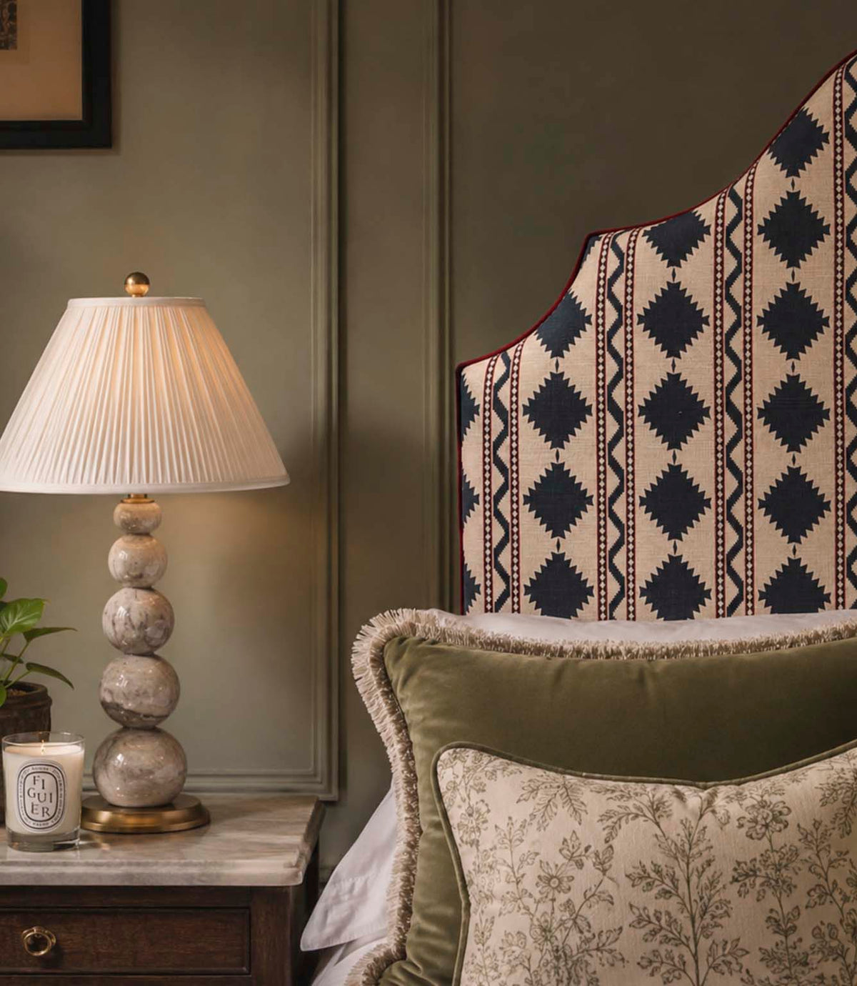 Arlo Geo Azure fabric upholstered statement headboard featuring a navy geometric floral stripe pattern on a natural background with burgundy piping, styled with layered cushions and a bedside lamp.
