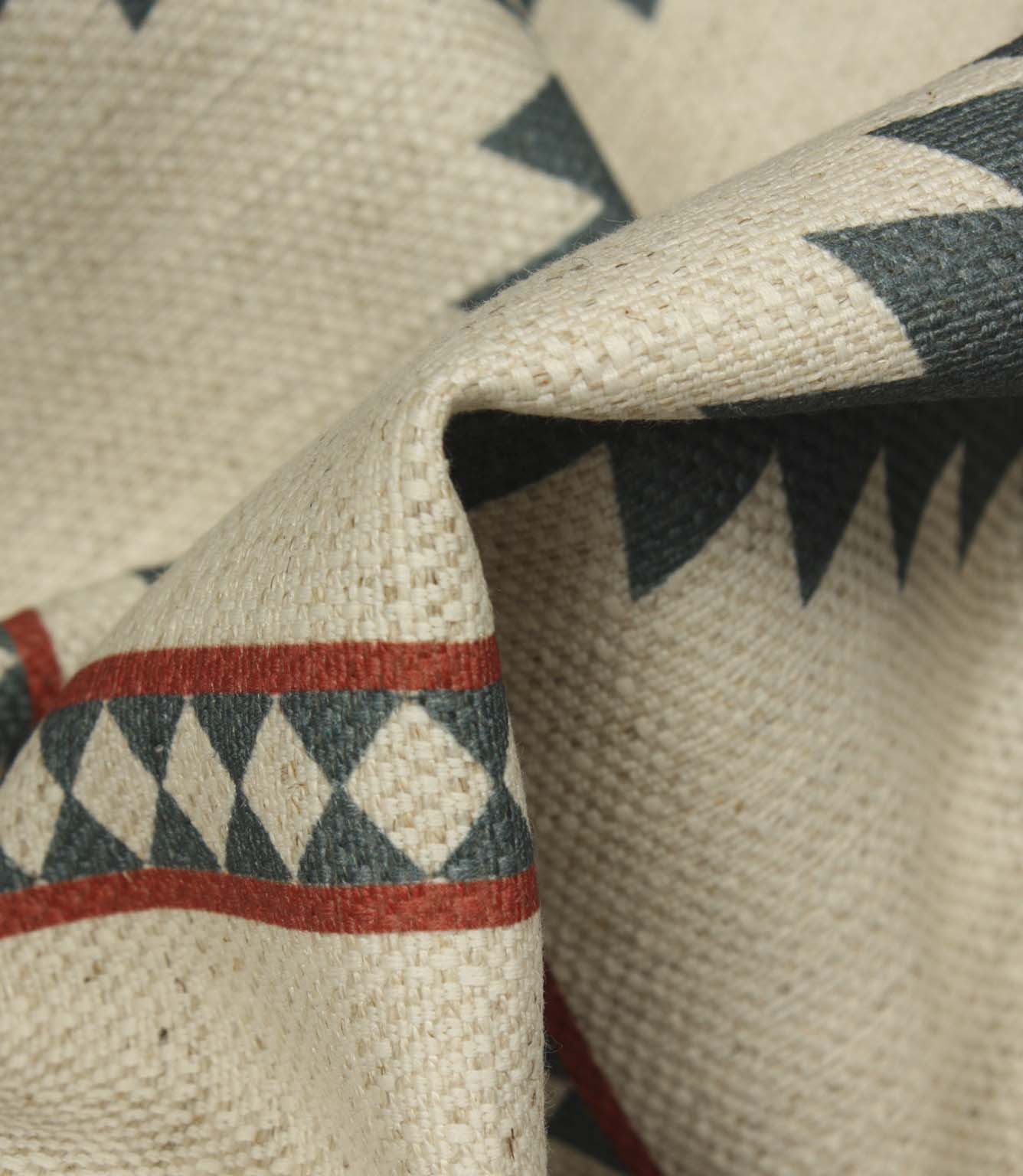 Macro close-up of cream woven fabric highlighting the textured weave, teal geometric border pattern, and rust red accent stripes.