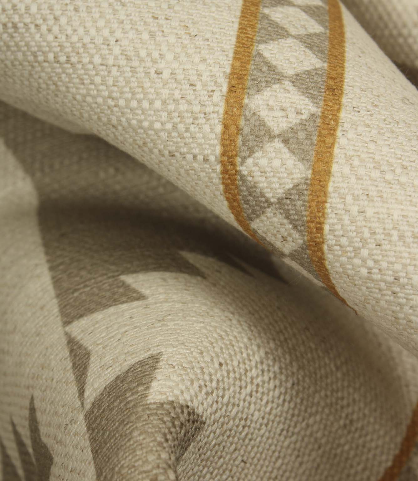 Close-up of cream woven fabric showing the soft drape, textured surface, taupe geometric motif and warm ochre border stripe detail.