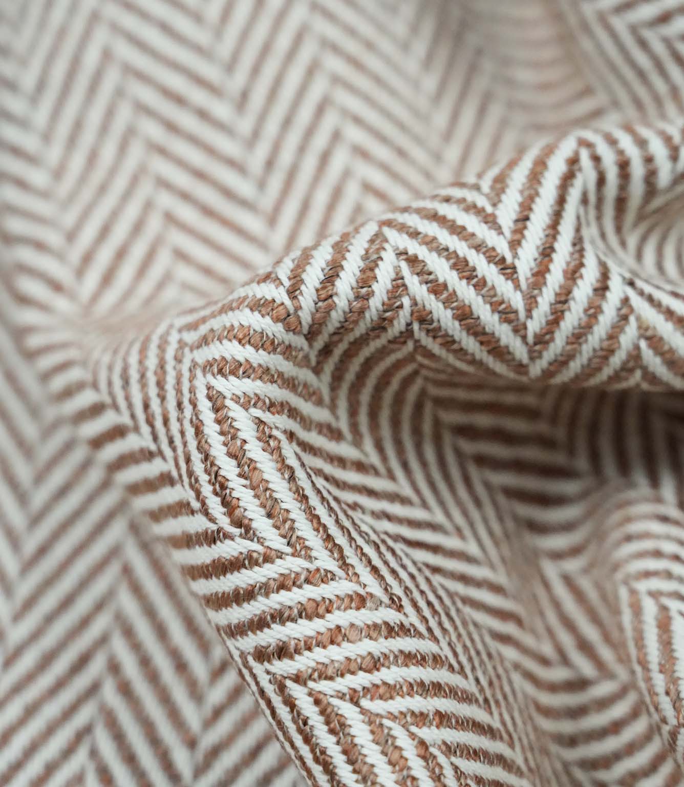 Detailed folded view of Bampton Terracotta herringbone upholstery fabric showing the depth of the woven chevron pattern, durable texture and soft finish for premium home furnishings.