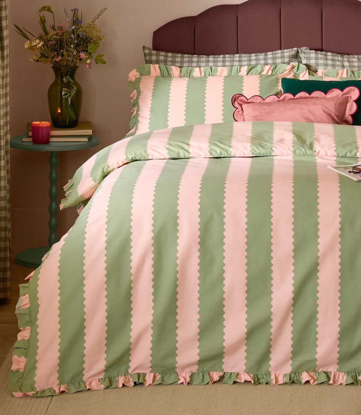 Birdie Stripe pink and green striped duvet cover and matching ruffled pillowcases, styled on a bed with decorative cushions and bedside flowers.