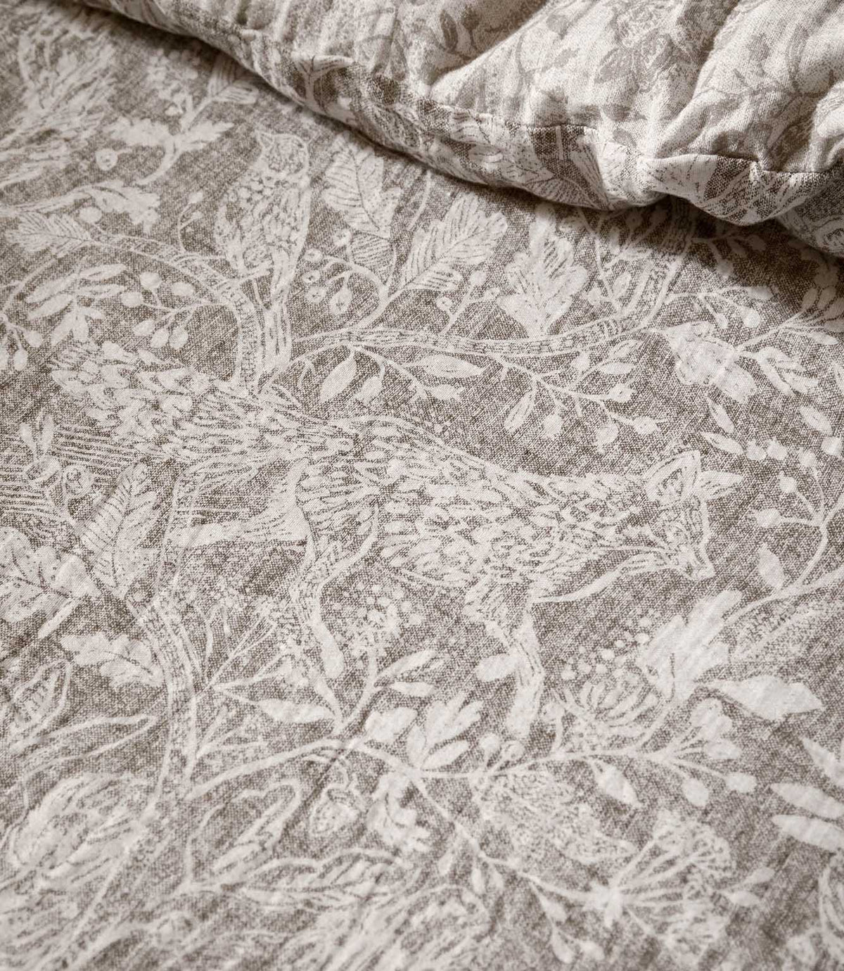 Close-up of Voyage Maison Cademuir bedding in Nut, showing the intricate grey-brown woodland print with birds, leaves, branches and botanical details.