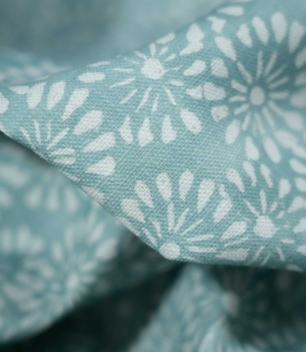 Macro photograph of Chamberry Duck Egg fabric showing the fine woven texture, soft duck egg blue-green background and delicate white floral motifs with rounded petals and fine radiating lines.