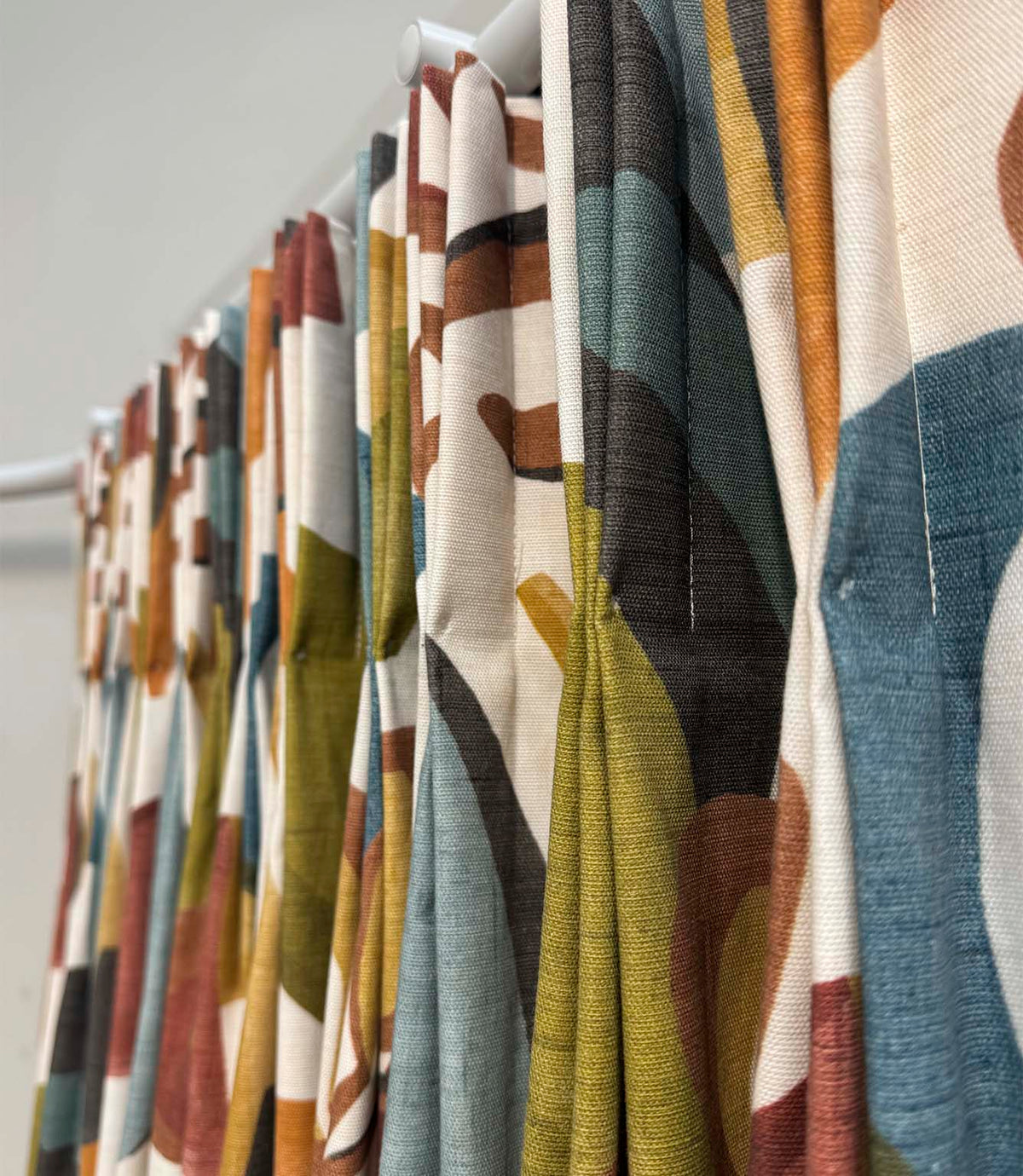 Angled close-up of Elaris Fabric Auburn curtains, showing the textured woven fabric and large-scale abstract botanical pattern in teal blue, olive green, burnt orange, rust and charcoal.