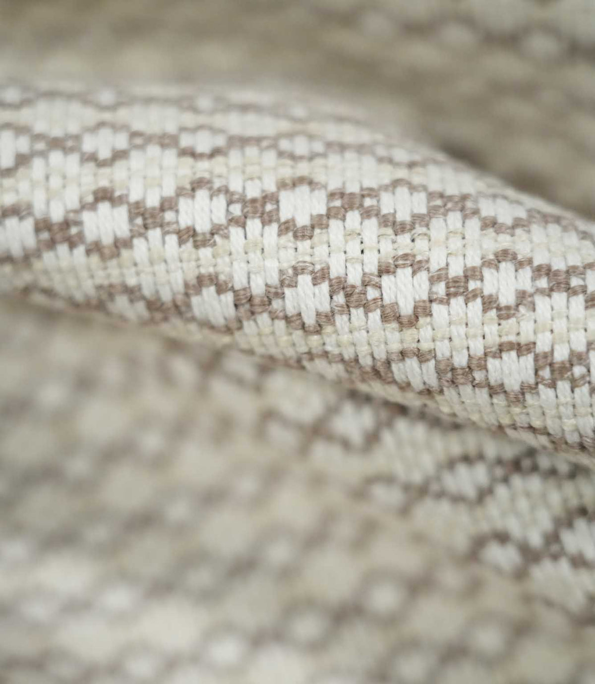 Extreme close-up of Elkstone Taupe fabric revealing interwoven cream and taupe yarns, a raised textured surface and repeating small-scale geometric motifs.