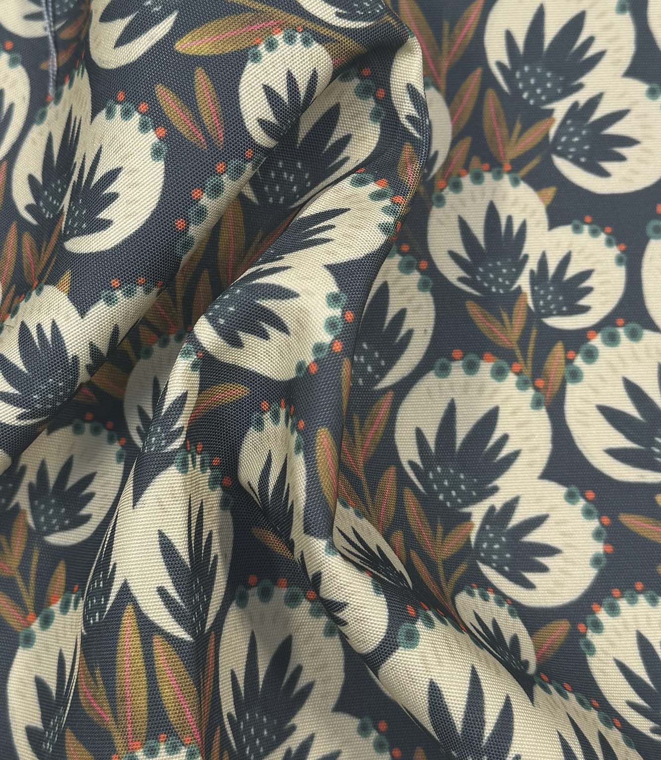 Draped Ember Crest outdoor upholstery fabric showing a decorative botanical pattern in navy, cream, coral, and olive shades.
