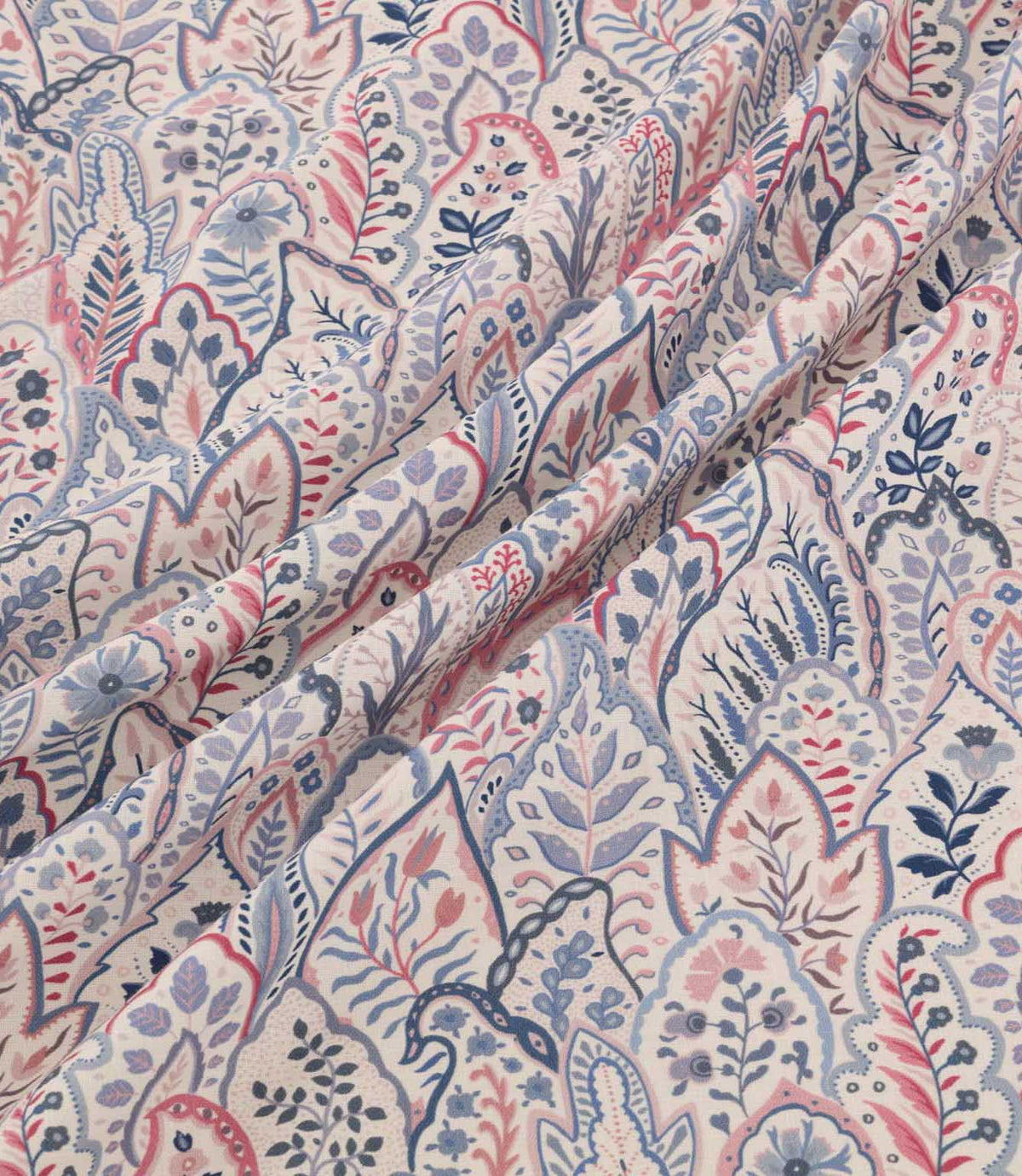 Hitherhill Anemone floral fabric arranged in soft, flowing folds, showcasing its detailed botanical design of layered leaf shapes, delicate flowers and decorative foliage in blush pink, muted blue, navy and lavender tones on an ivory background.