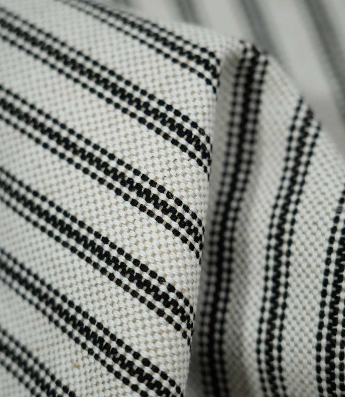 Detailed close-up of folded black ticking stripe fabric showing the natural cream weave and fine black stripes following the soft folds of the material.