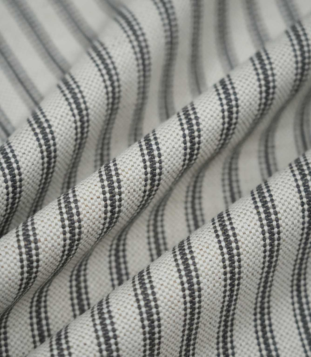 Grey ticking stripe fabric arranged in soft folds, showing how the classic charcoal striped pattern follows the drape of the textured woven fabric.