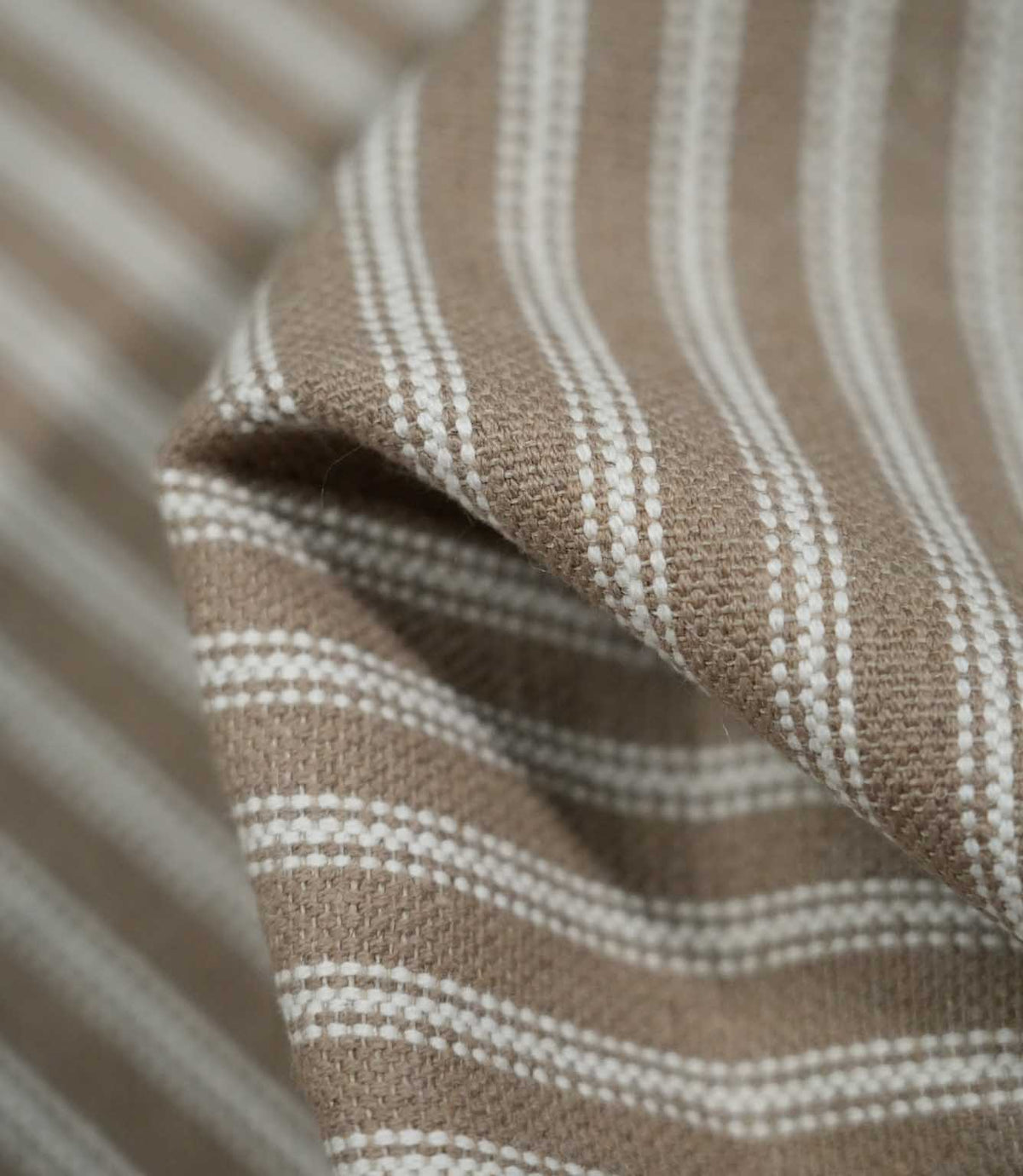 Detailed close-up of draped natural ticking stripe fabric with ivory woven stripes on a warm taupe-beige ground, highlighting its texture and flexible drape.