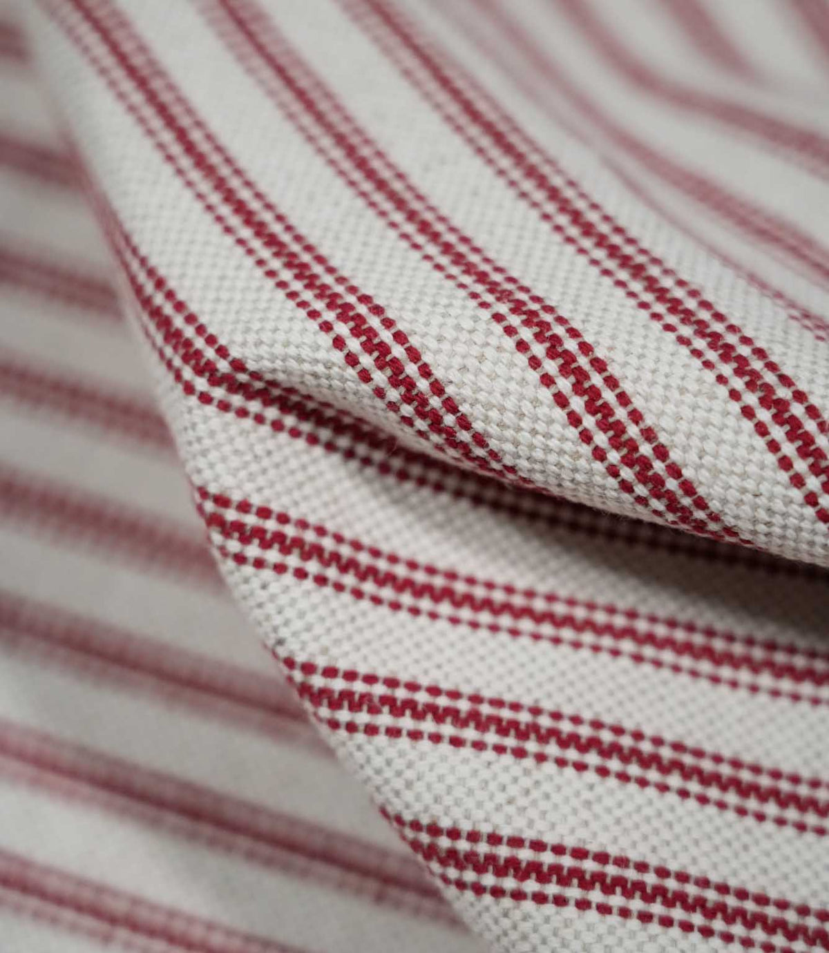 Detailed close-up of draped red ticking stripe fabric, highlighting the narrow red stripes, natural cream woven background and tactile textured weave.