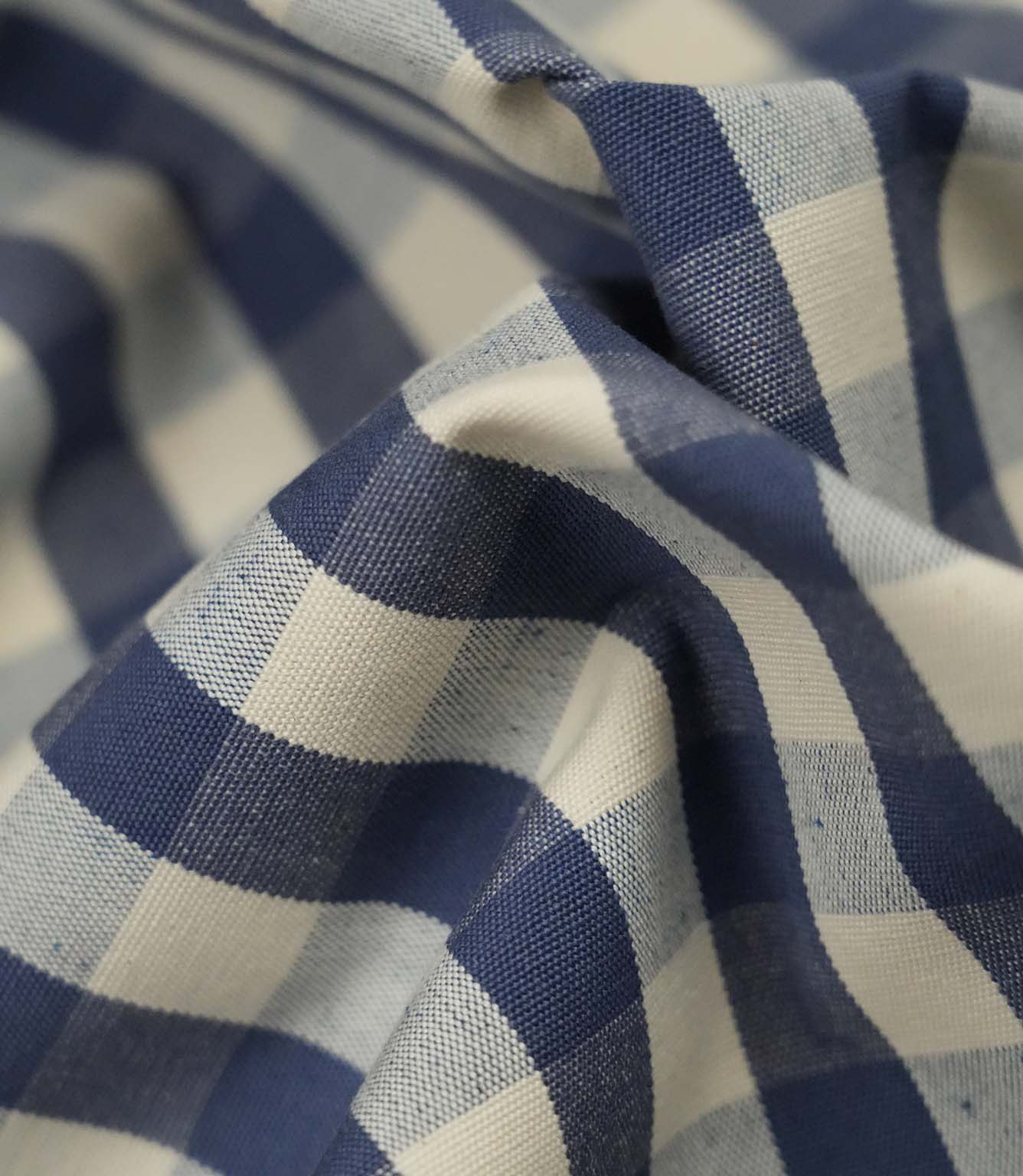 Close-up detail of blue and ivory small gingham fabric showing the fine weave, soft texture and classic checked pattern.