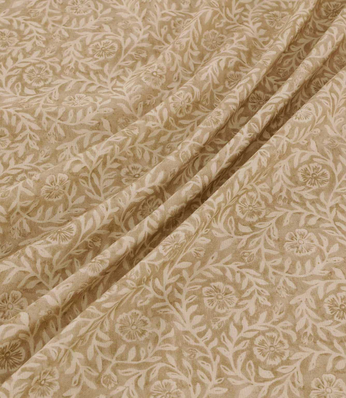 Manorville Dune floral fabric arranged in soft, flowing folds, showcasing its warm sandy beige background, delicate cream flowers and winding leafy stems, with the intricate botanical pattern continuing across the draped fabric.