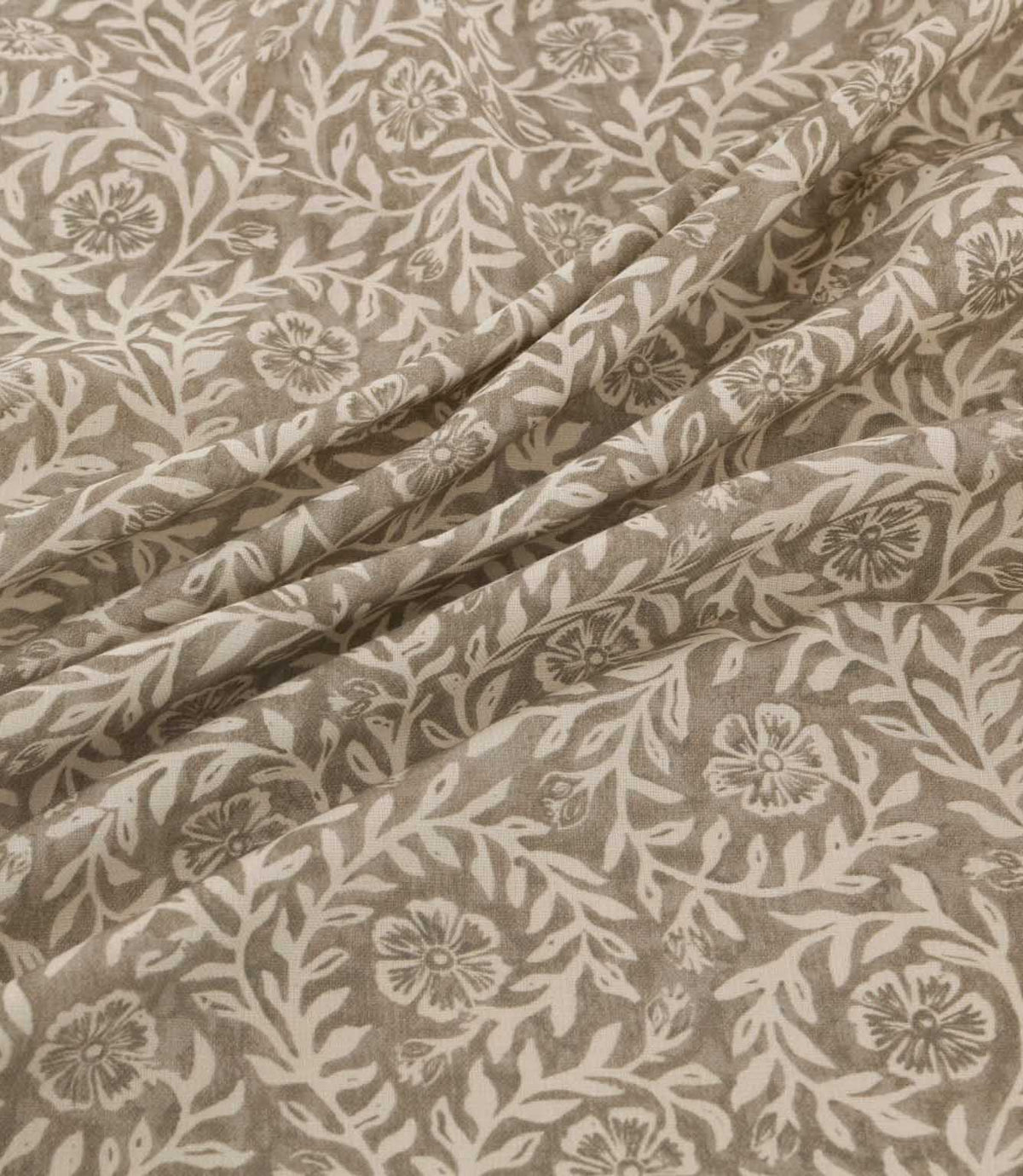 Manorville Quaker fabric arranged in soft, flowing folds, showcasing its intricate ivory floral and foliage design on a warm taupe background, with detailed blossoms, winding stems and a natural woven texture.