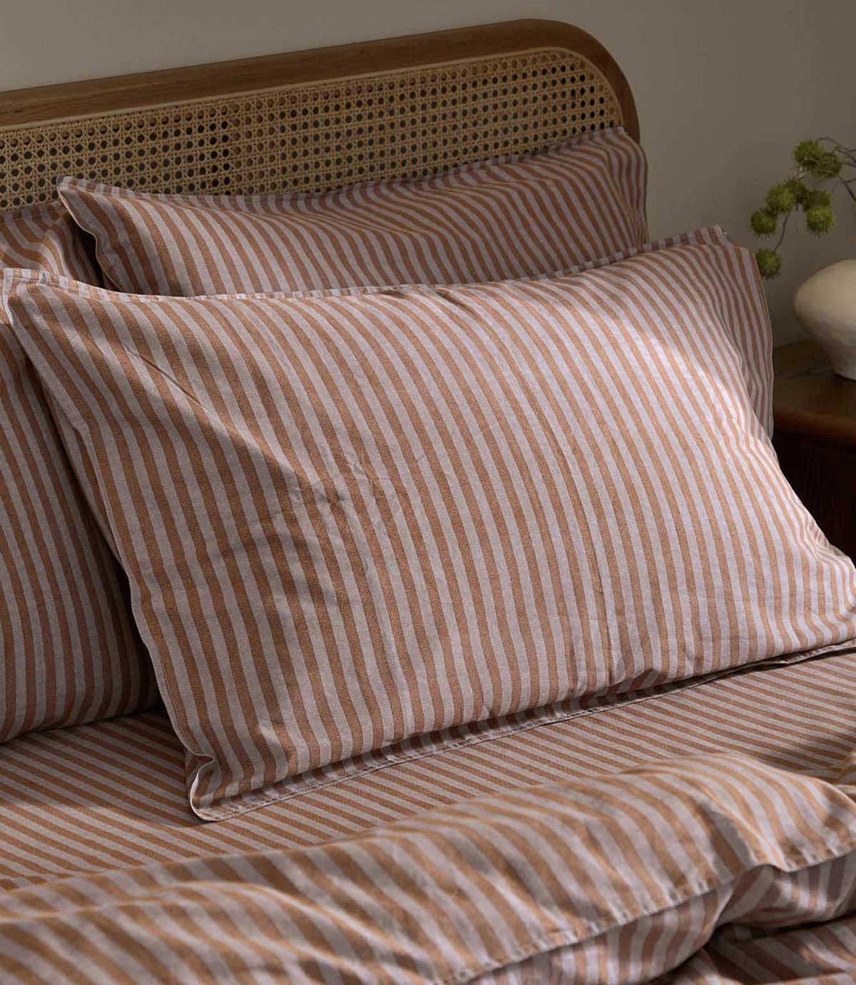 Close-up of Marlow Stripe pillowcases in Cocoa/Vintage Blue showing the alternating cocoa brown and soft vintage blue stripes, with matching bedding and a cane headboard.