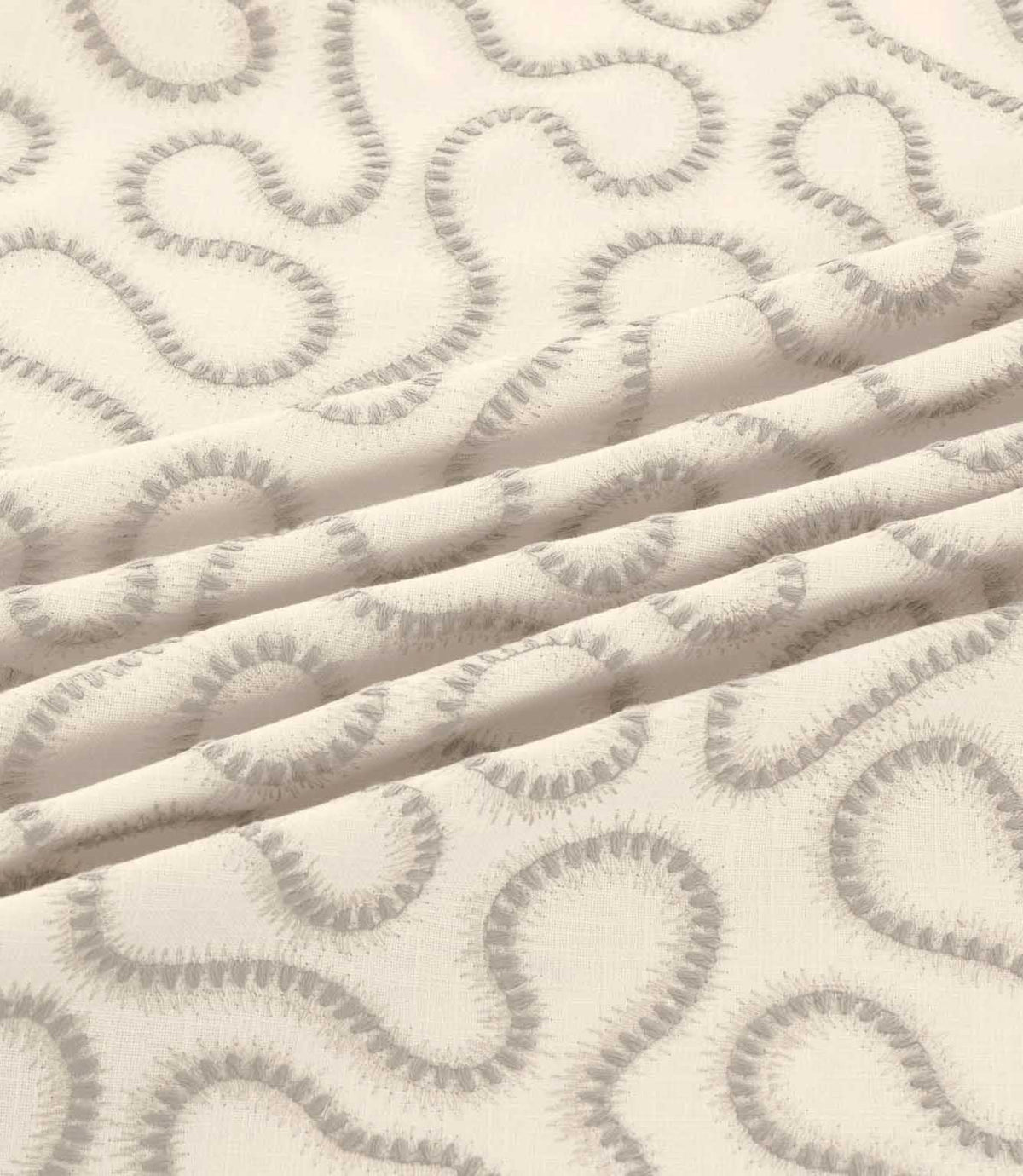 Orient Gull fabric gathered into gentle folds, highlighting its soft grey embroidered abstract pattern and textured ivory woven background.