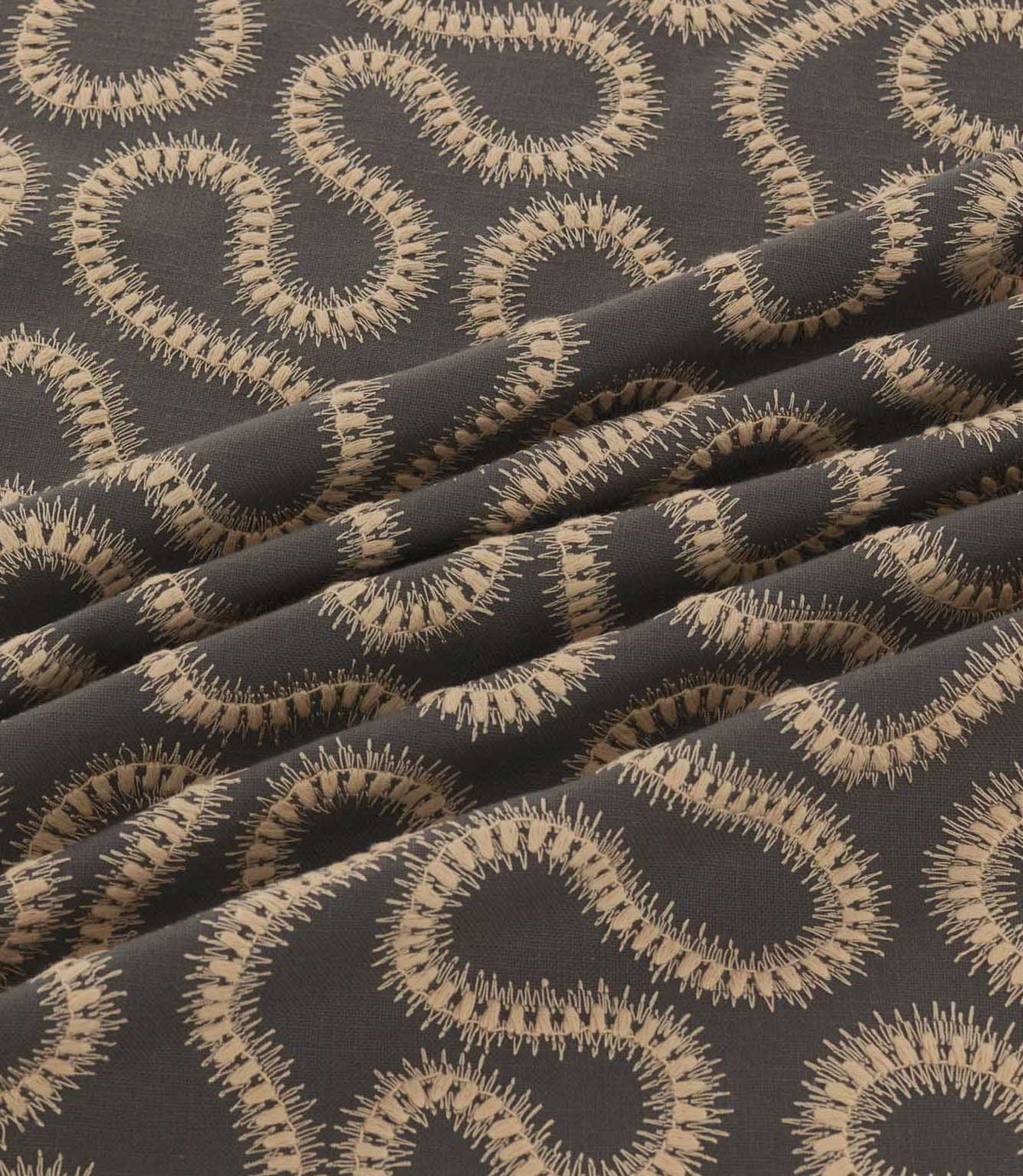 Orient Rockport embroidered fabric arranged in soft folds, showing detailed beige wavy stitching against a contrasting charcoal woven background.