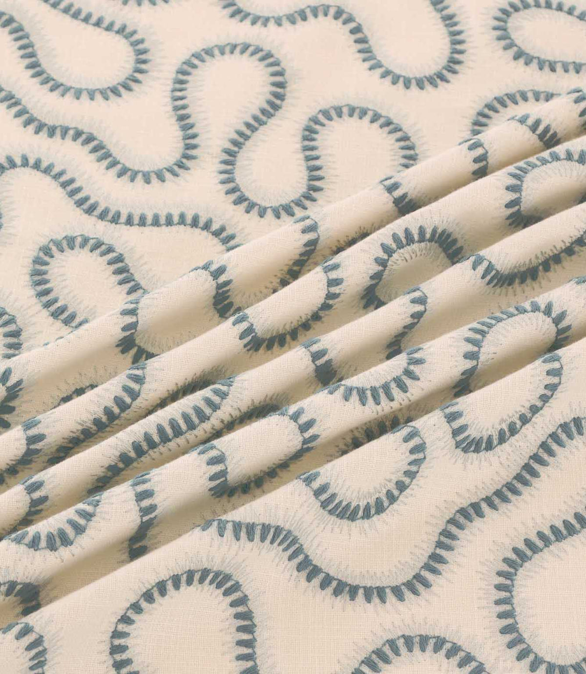 Close-up of Orient Saltwater fabric draped in folds, featuring muted blue embroidered squiggle patterns on a soft cream woven background.
