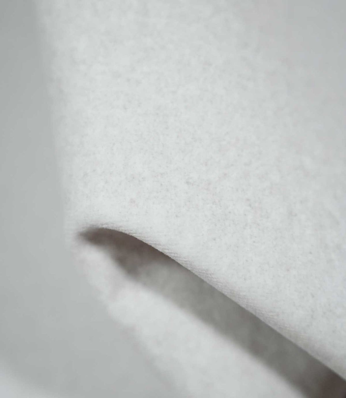 Detailed close-up of Palermo Marble light grey upholstery fabric folded over itself, revealing its softly brushed surface, fine mottled fibres and smooth, rounded fold.