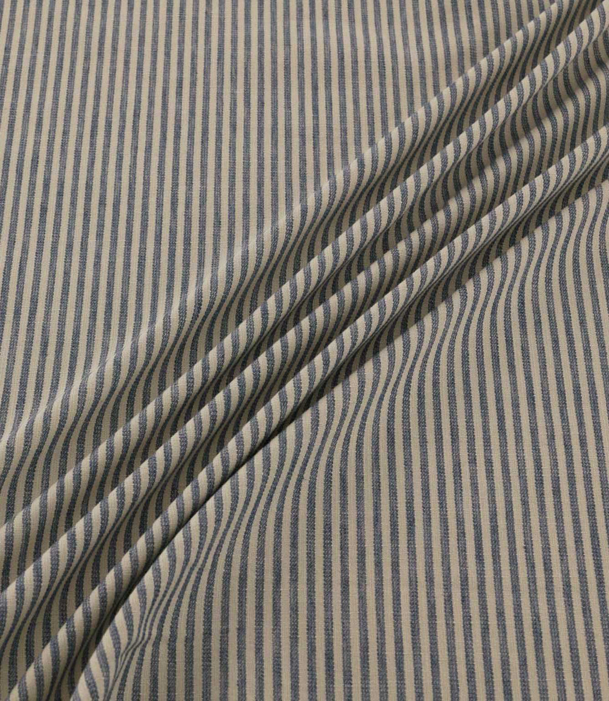 Shoreham Nautica fabric draped in soft diagonal folds, showcasing its narrow navy blue and cream ticking stripes, textured woven finish and natural drape.
