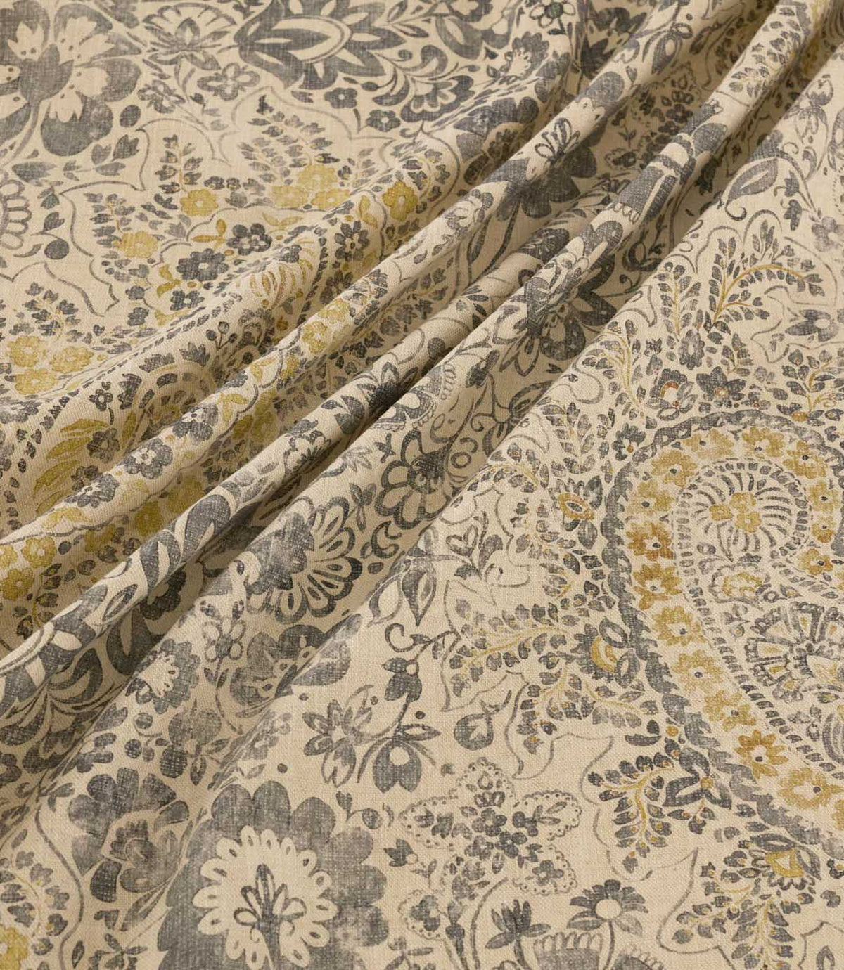 Southold Rockport fabric draped in soft diagonal folds, showcasing its detailed charcoal grey, olive and mustard yellow paisley floral pattern, trailing botanical foliage and textured natural cream background.