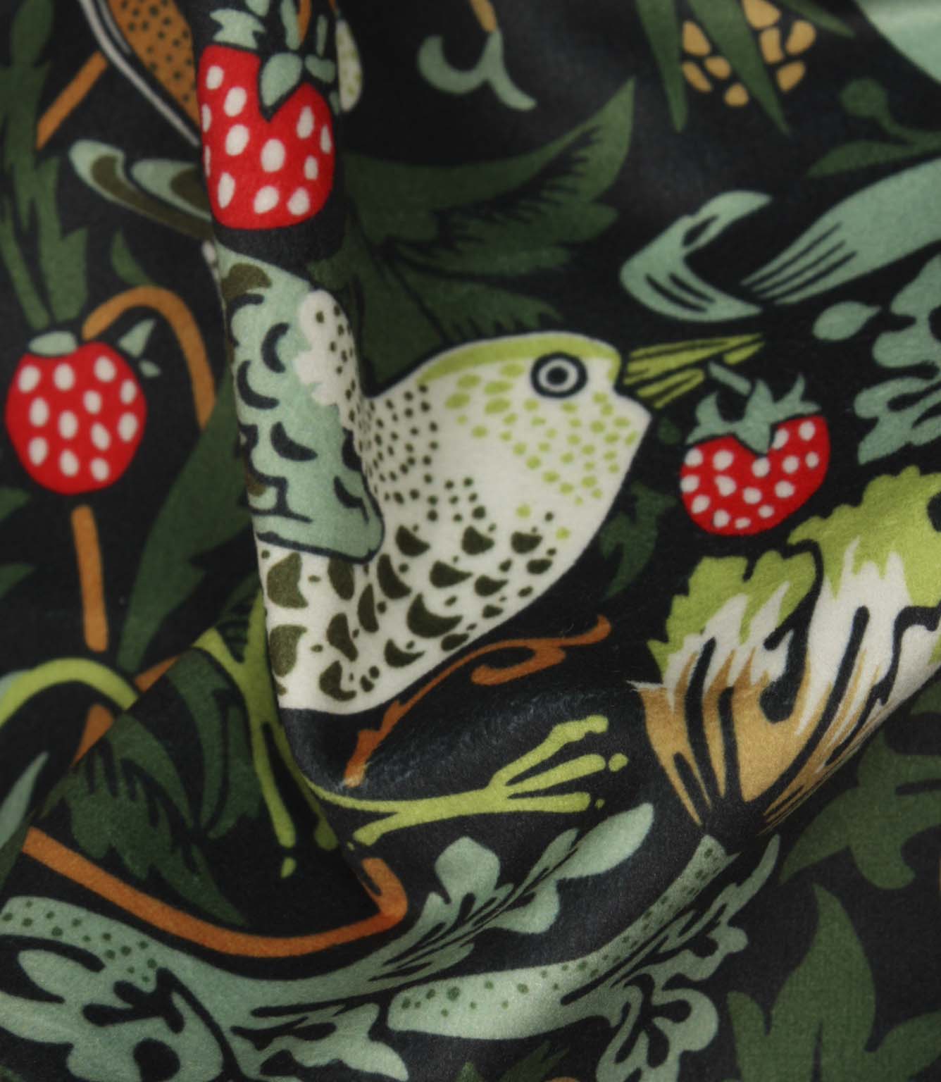 Detailed close-up of bird motif on black botanical fabric with bright red strawberries and soft green leaves.