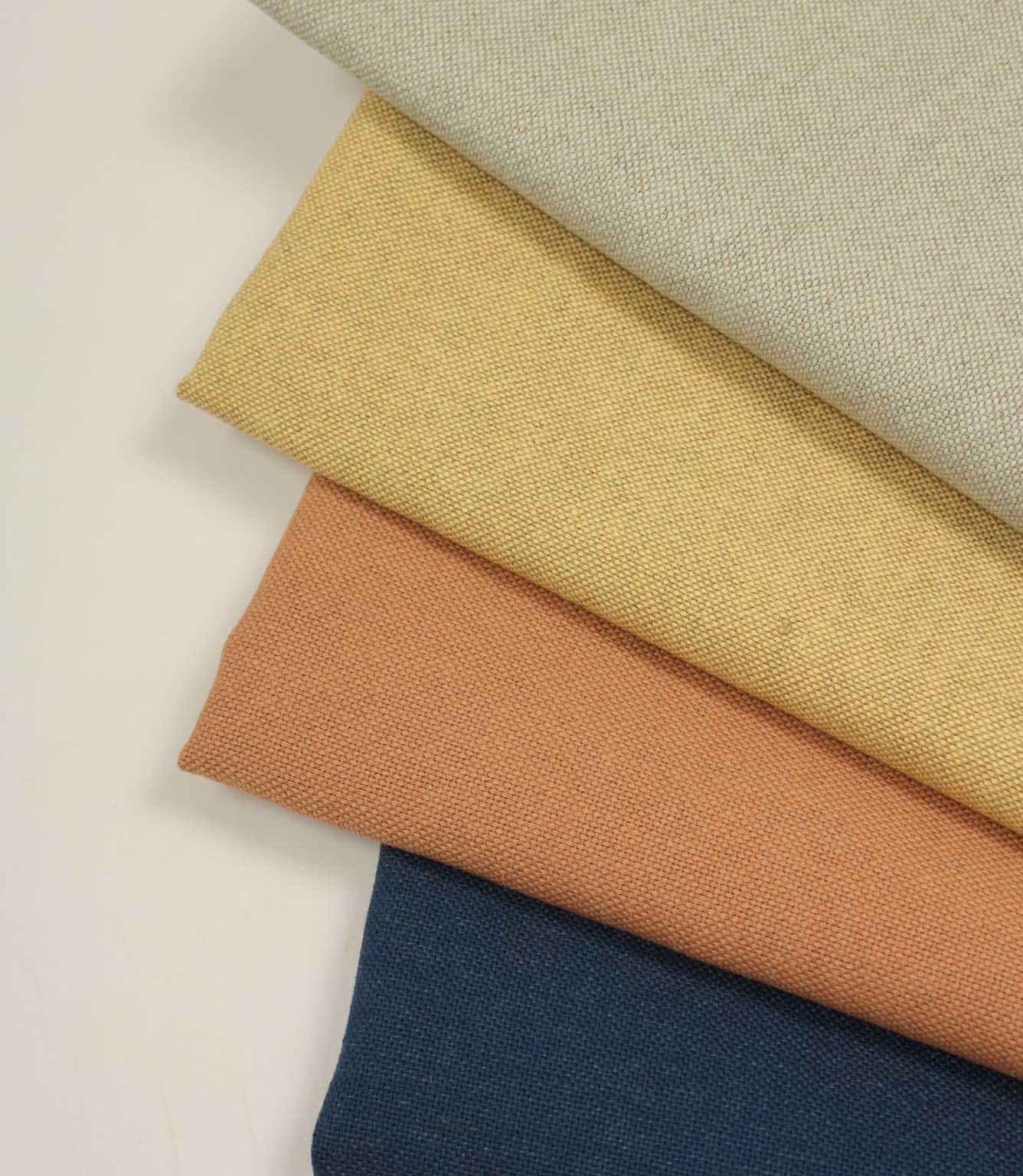 Close-up stack of woven fabrics in beige, orange, yellow and blue.