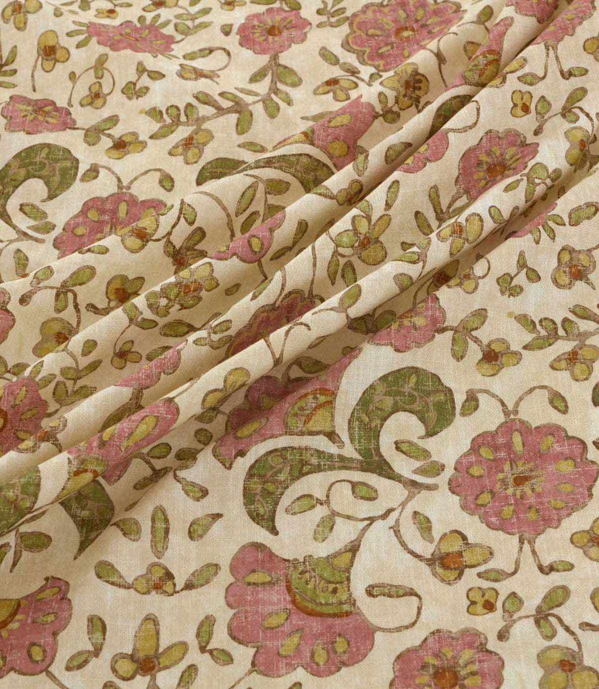 Wainscott Rosehip floral upholstery and curtain fabric arranged in soft diagonal folds, showcasing its traditional botanical design of pink flowers, olive green foliage and golden ochre blossoms against a warm ivory background, with a softly textured woven appearance.