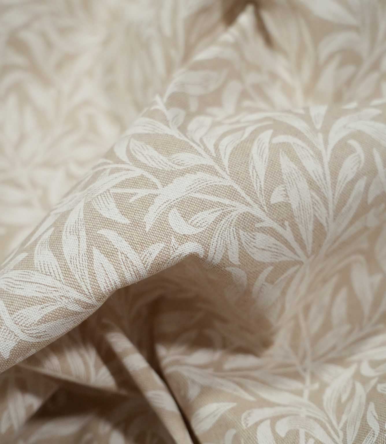 Close-up of draped Willow Bough Linen Look fabric in beige and cream, highlighting the flowing leaves, woven texture and natural movement of the material.