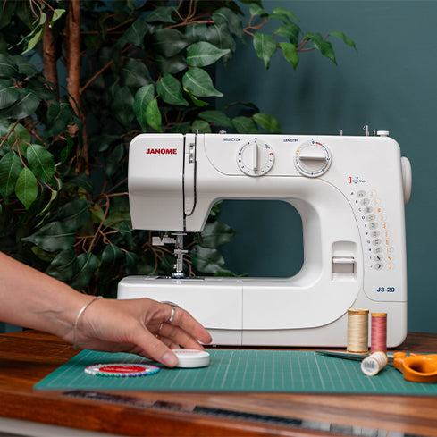 Sewing machine with a hand coming in from the left of the image. 