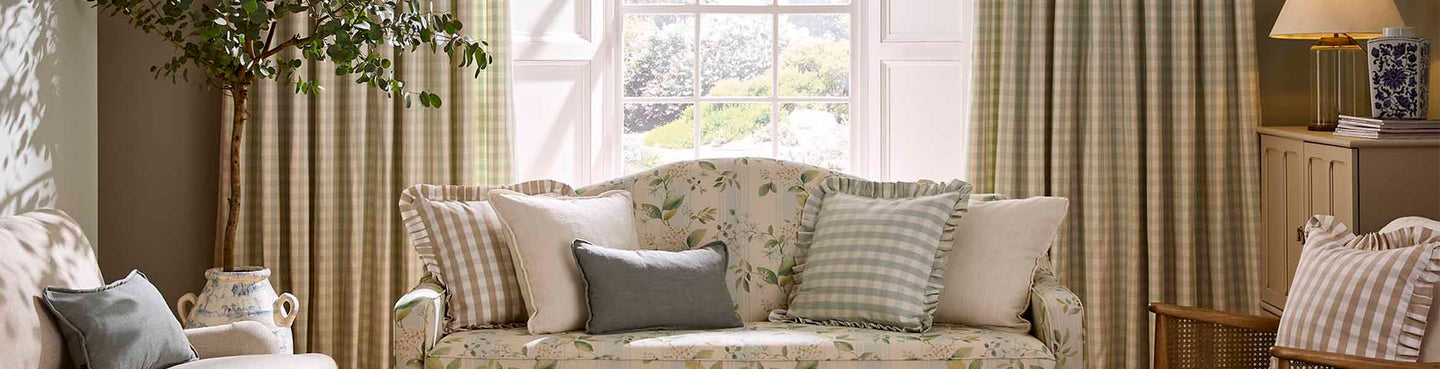 Light, airy sitting room with green check curtains, a floral upholstered sofa, and a mix of striped and plain cushions creating a soft, country-inspired look.