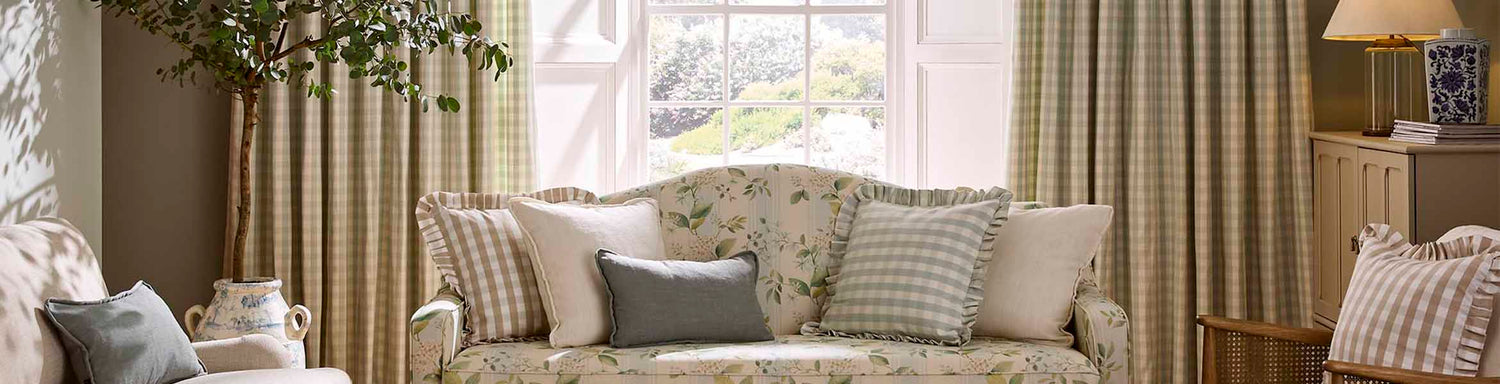 Light, airy sitting room with green check curtains, a floral upholstered sofa, and a mix of striped and plain cushions creating a soft, country-inspired look.