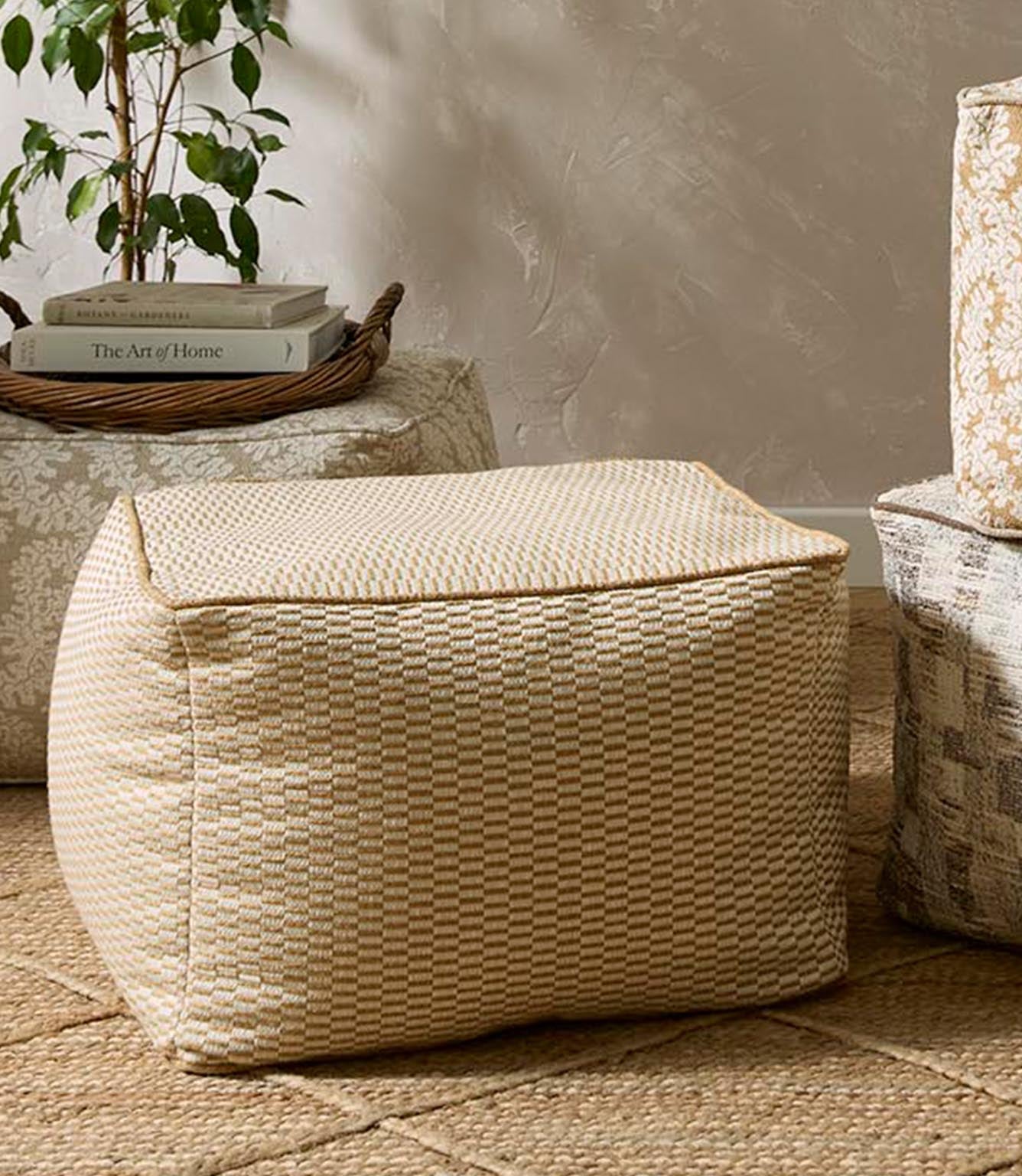 Neutral upholstered pouffe in a small-scale woven pattern, styled in a relaxed living space with natural textures, a jute rug and soft-toned furnishings.