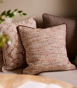 Upholstered bench seating styled with textured woven cushions in warm neutral and terracotta tones, paired with patterned fabrics in a cosy dining nook.