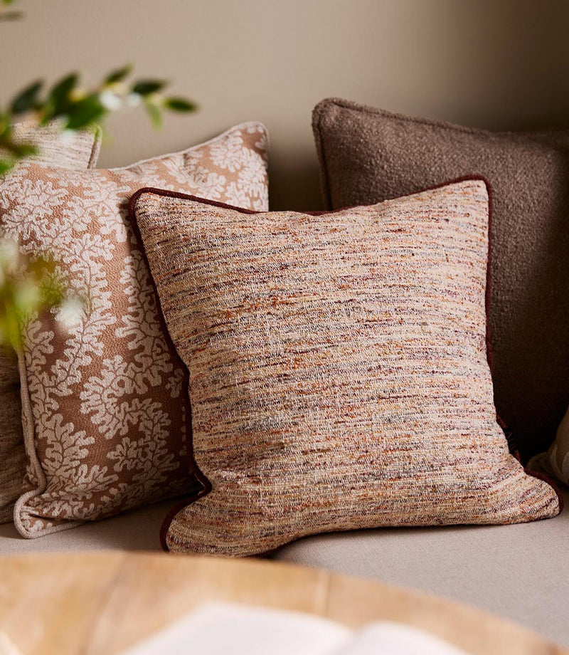 Upholstered bench seating styled with textured woven cushions in warm neutral and terracotta tones, paired with patterned fabrics in a cosy dining nook.