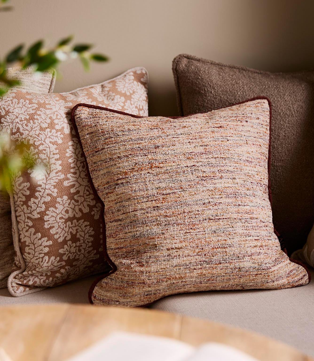 Upholstered bench seating styled with textured woven cushions in warm neutral and terracotta tones, paired with patterned fabrics in a cosy dining nook.