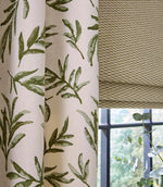 Detailed view of embroidered green leaf curtain fabric alongside a small-scale geometric Roman blind, styled with a window and fresh greenery for a relaxed, cohesive look.