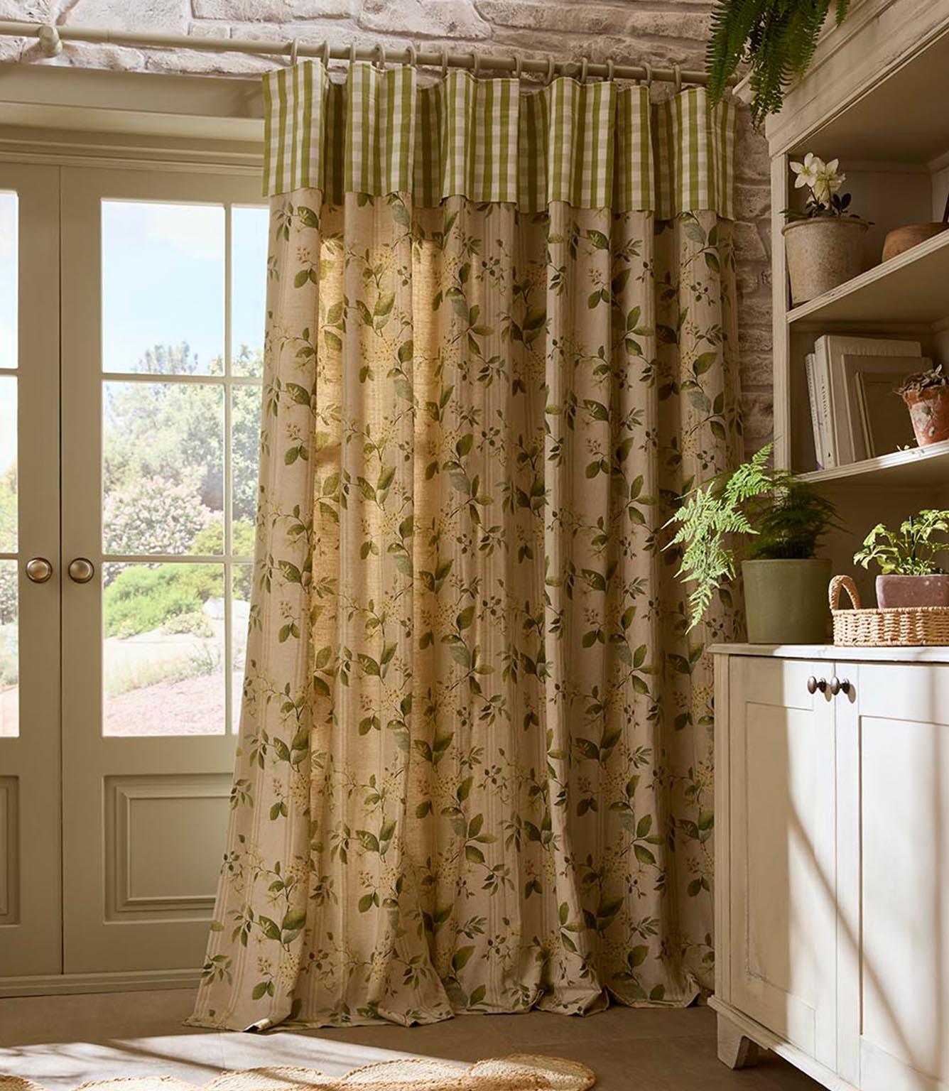 Country-style curtains in a soft botanical print with green leaves and delicate blossoms, finished with a green gingham header, hanging beside a glazed door in a light-filled room.
