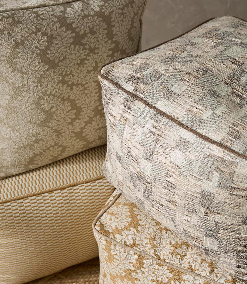 Upholstered cushions in a woven foliage fabric in soft beige and ivory tones, styled alongside complementary textured upholstery fabrics.
