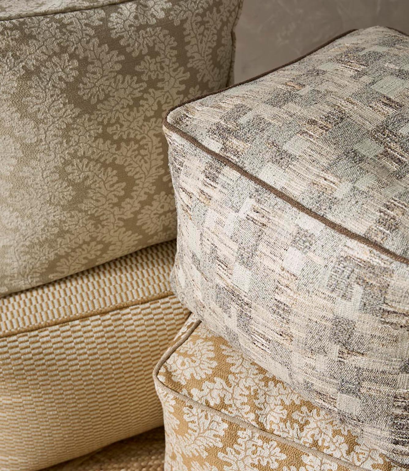 Upholstered cushions in a woven foliage fabric in soft beige and ivory tones, styled alongside complementary textured upholstery fabrics.