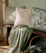 Interior setting with cushions in soft green and neutral upholstery fabrics on a wooden bench, paired with a draped throw and natural accessories for a relaxed, contemporary look.