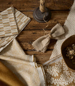 Flat lay of coordinated upholstery fabrics in warm neutral and ochre tones, showing a mix of woven textures and patterns on a rustic wooden surface with styling accessories.