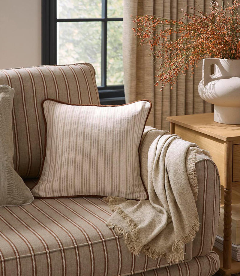 Striped upholstered armchair with coordinating cushion and soft throw, styled in warm neutral tones alongside woven curtains and natural wood accents.