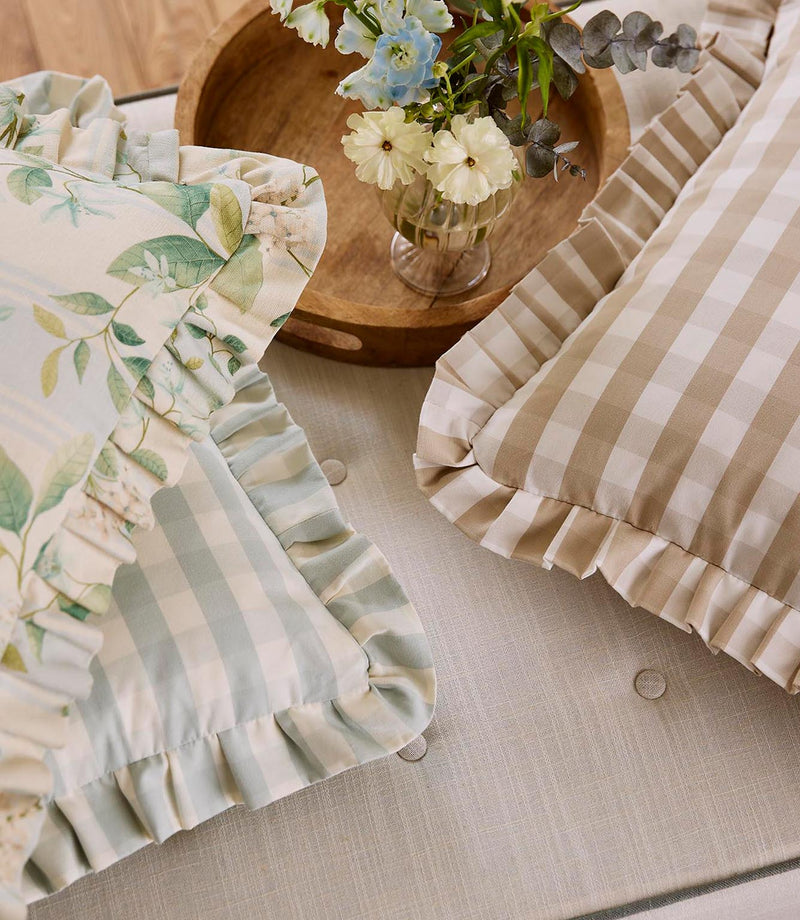 Close-up of decorative cushions combining botanical print and soft stripe fabrics, finished with gathered ruffle trims in muted green and neutral tones.