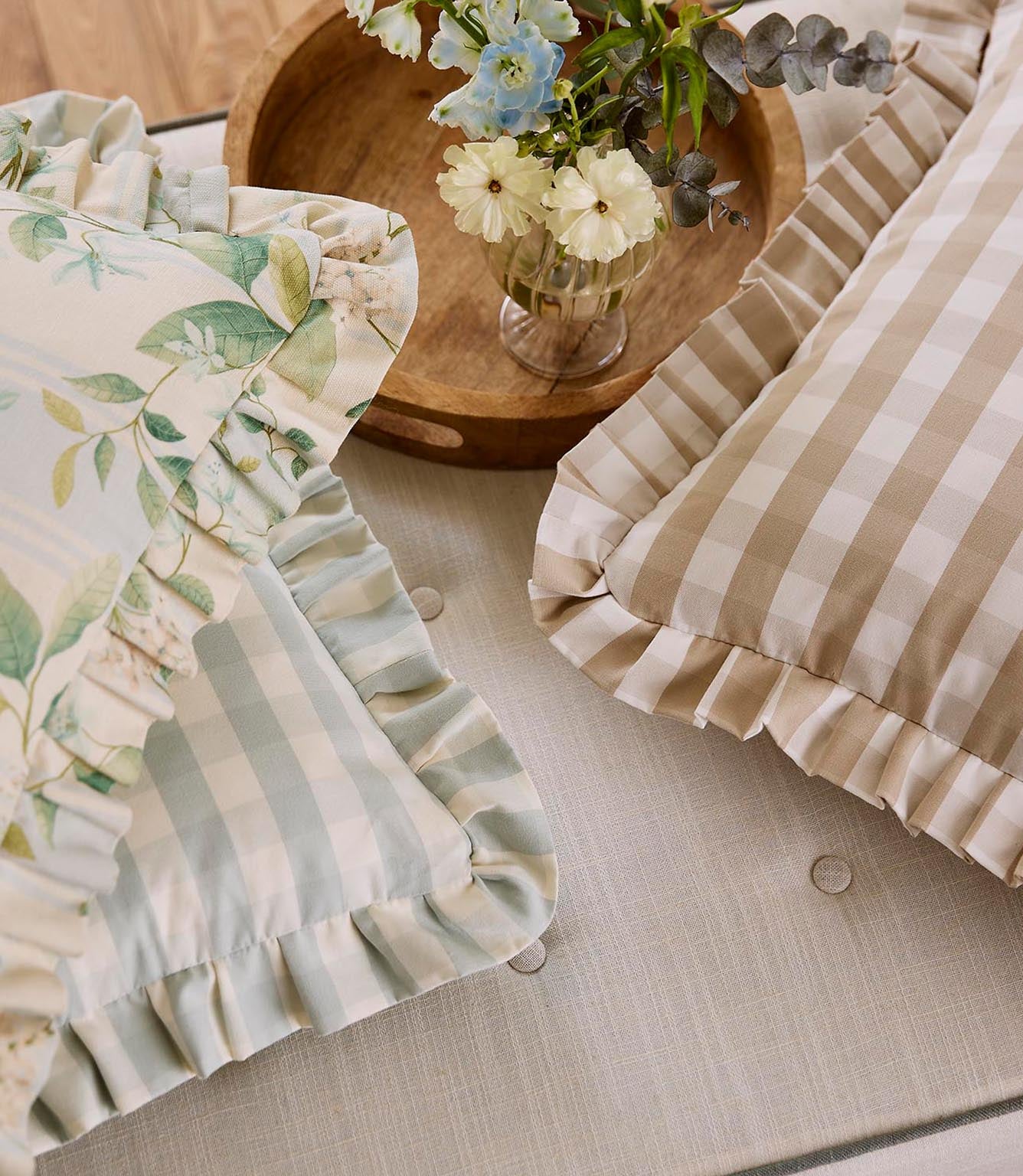 Close-up of decorative cushions combining botanical print and soft stripe fabrics, finished with gathered ruffle trims in muted green and neutral tones.
