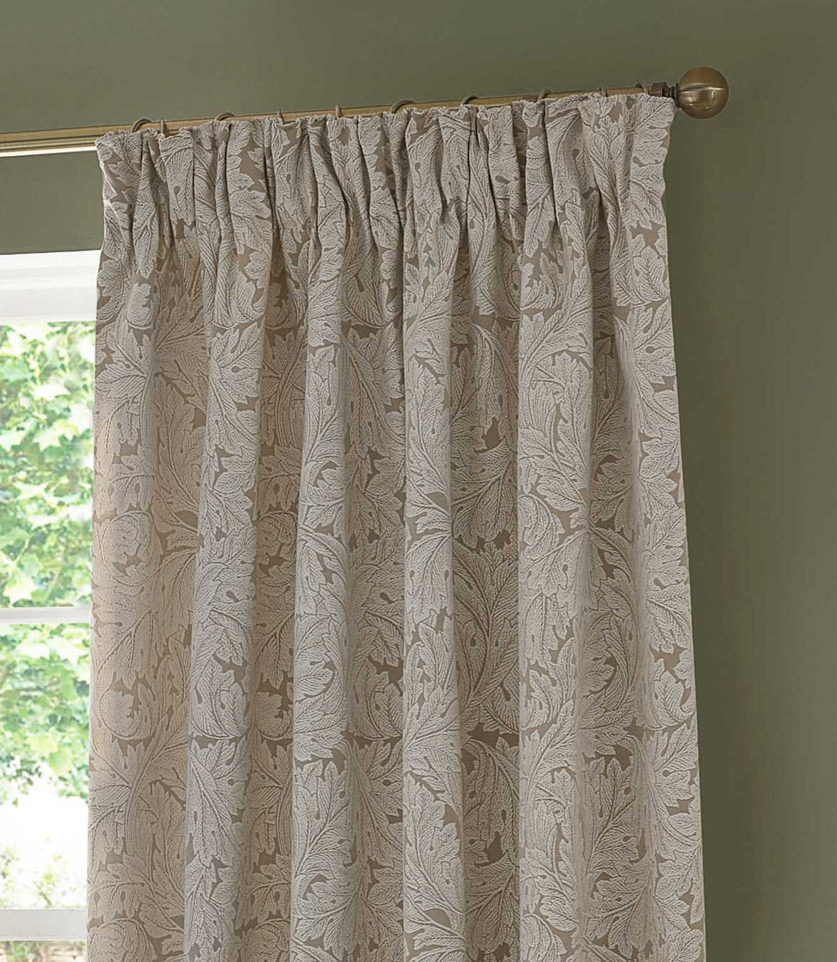 Morris & Co Acanthus jacquard curtain in cream and warm beige, showing the gathered pencil pleat heading and detailed woven leaf pattern against a green wall.