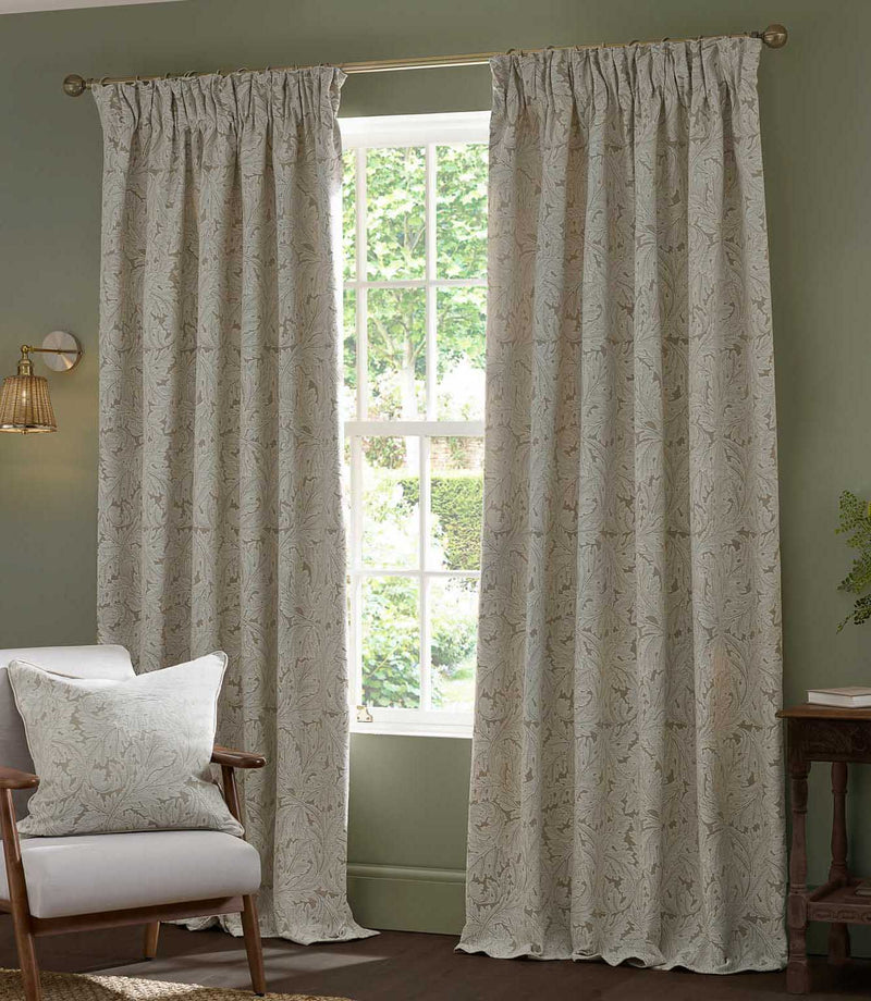 Pair of full-length Morris & Co Acanthus jacquard curtains in cream and warm beige framing a tall window, styled in a traditional living room with green walls and wooden furniture.